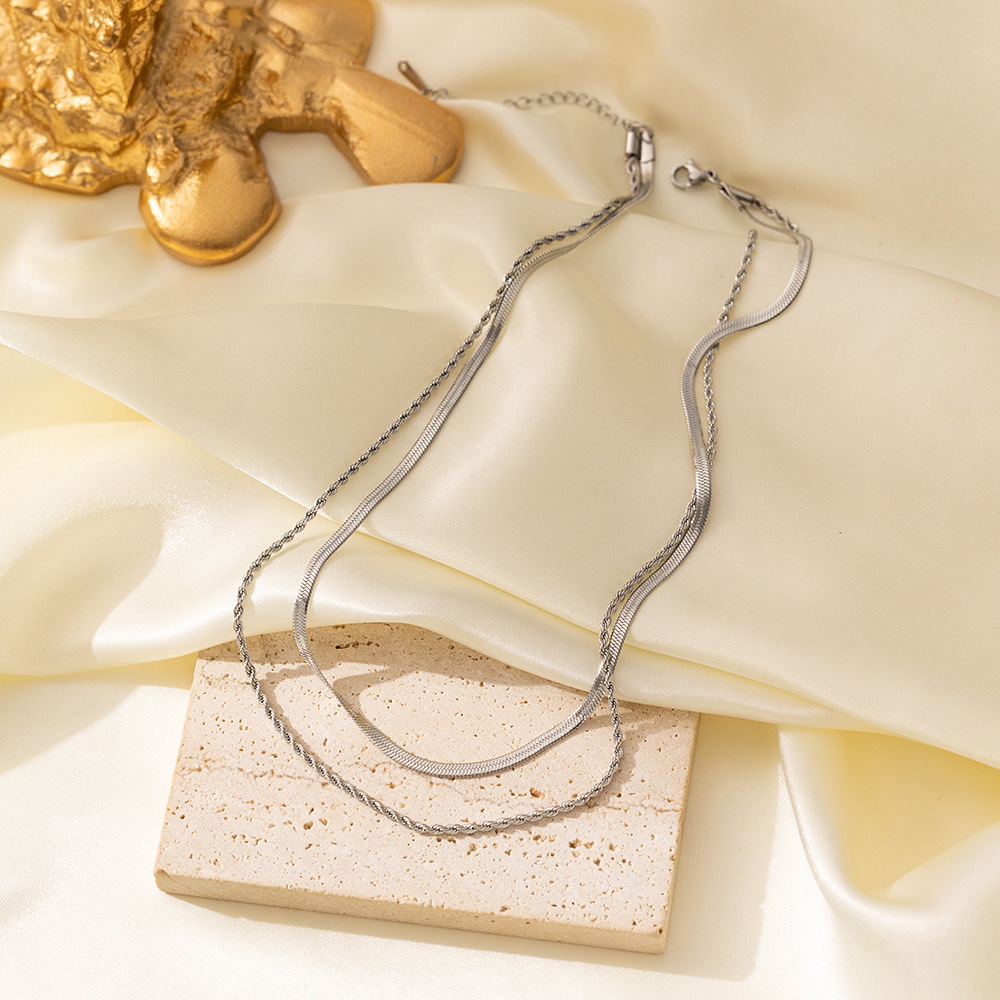 Silver-tone herringbone and rope chain necklace laid on cream satin and a stone block