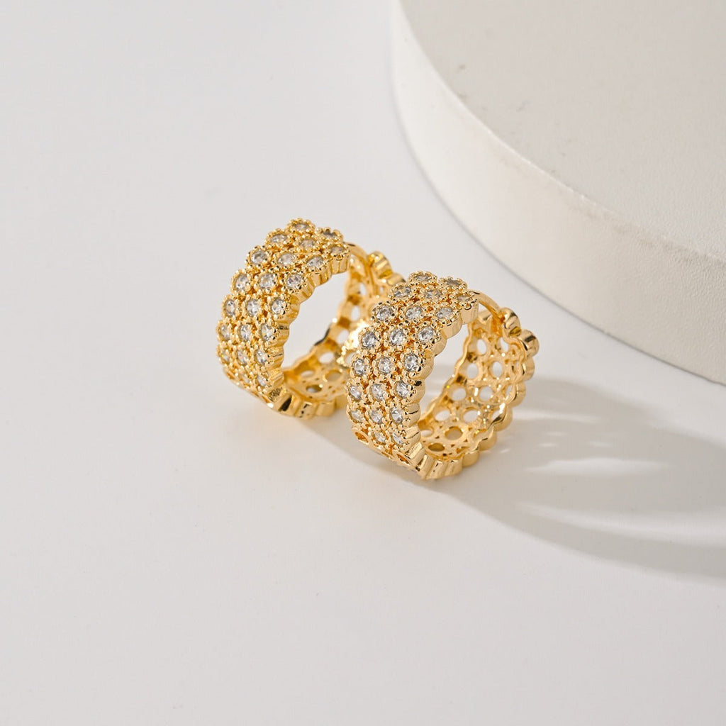 Gold-tone huggie hoops with three rows of clear zircons, beside a round white stand