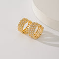 Gold-tone huggie hoops with three rows of clear zircons, beside a round white stand