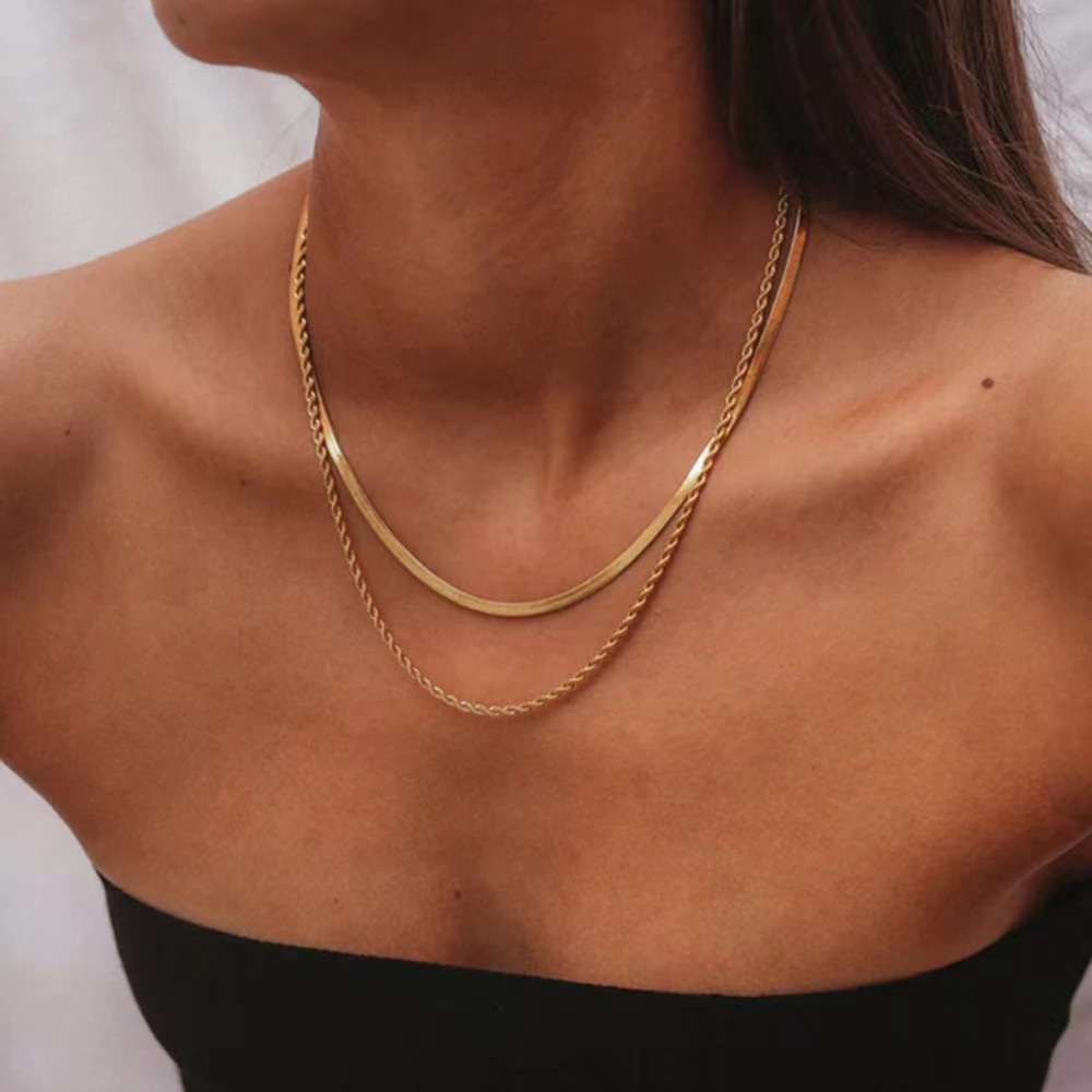 Gold-tone double-layer herringbone and rope chain necklace worn on the neck with a black top