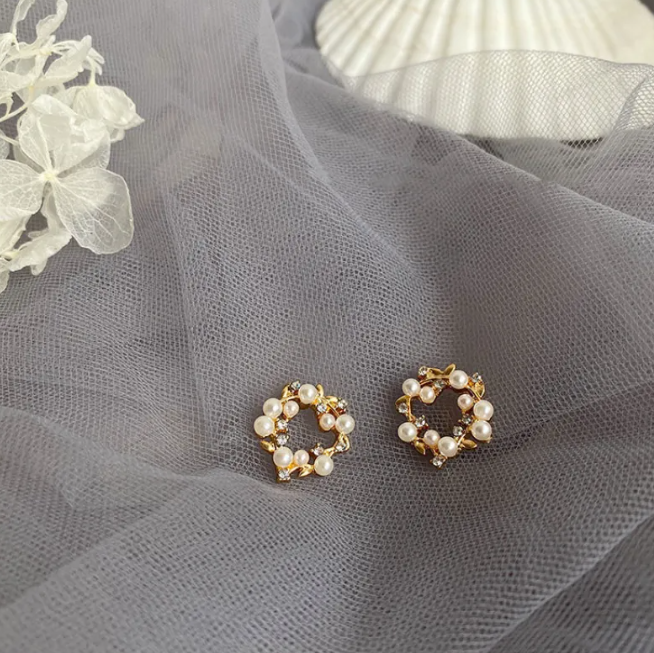 Pair of small wreath stud earrings with pearl-style beads and gold-tone details on grey tulle
