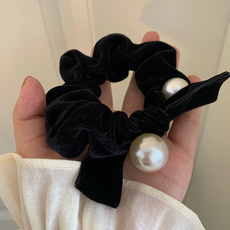 Black velvet-look bow scrunchie with pearl-style beads held in an open hand