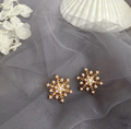 Pair of gold-tone snowflake earrings with pearl-style beads and small clear stones on grey tulle