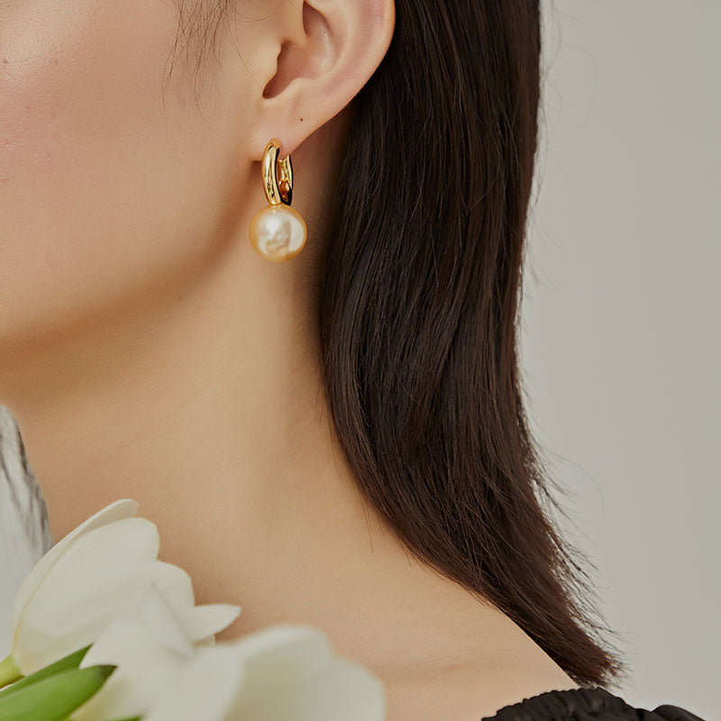 Gold-tone huggie hoop earring with white pearl-style drop, worn