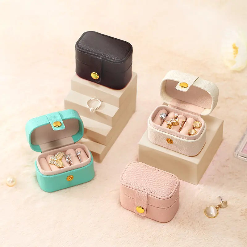 Black, cream, aqua and pink mini ring travel cases on display blocks, two open with rings