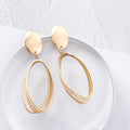 Gold-tone oval drop earrings with matte oval disc tops and layered open-oval wire drops, on a clear acrylic disc