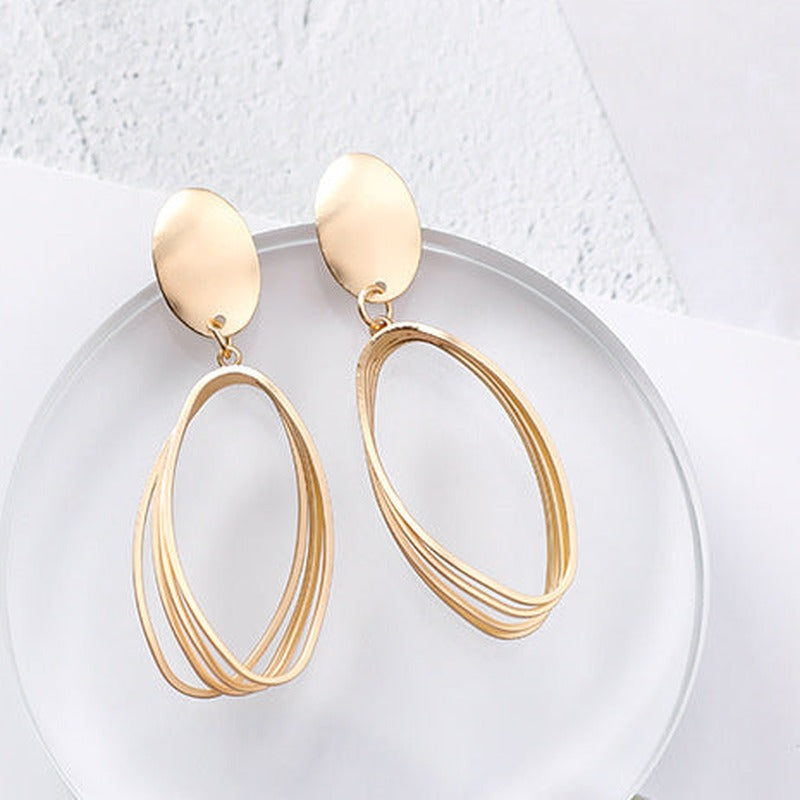 Gold-tone oval drop earrings with matte oval disc tops and layered open-oval wire drops, on a clear acrylic disc